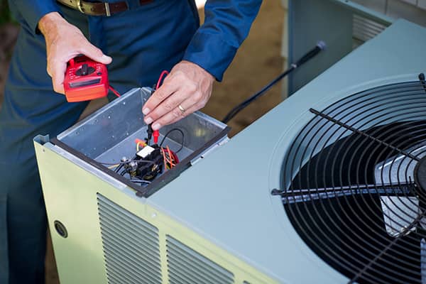 A man repairs an air conditioner, focused on his work with tools in hand.