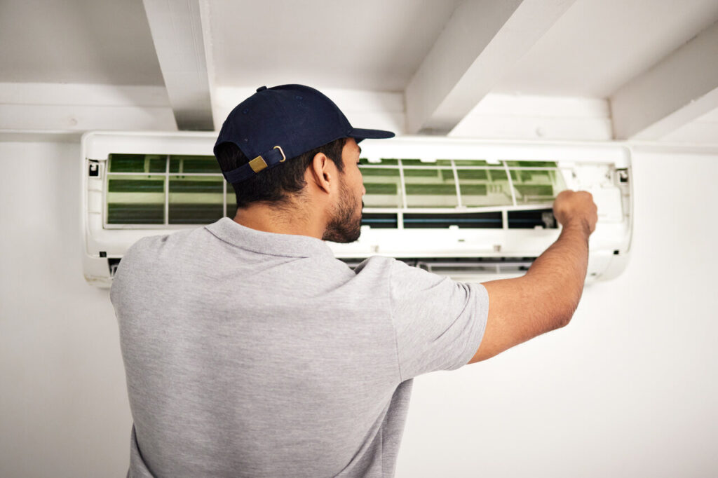 A man in a cap and shirt repairs an air conditioner.