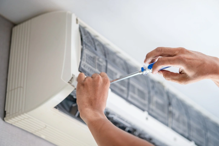 A person repairing an air conditioner, focused on the unit with tools in hand.